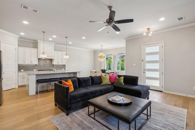 living room with ceiling fan with notable chandelier, light wood-type flooring, and ornamental molding