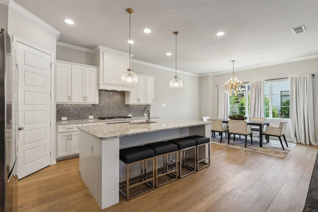 kitchen featuring white cabinets, a center island with sink, light stone counters, and light hardwood / wood-style flooring