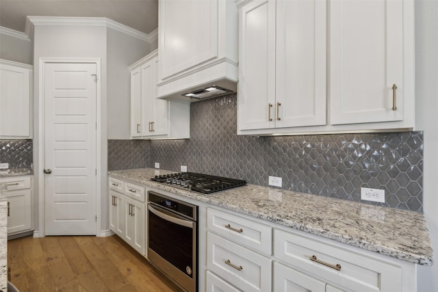 kitchen featuring white cabinetry, stainless steel appliances, light wood-type flooring, decorative backsplash, and ornamental molding