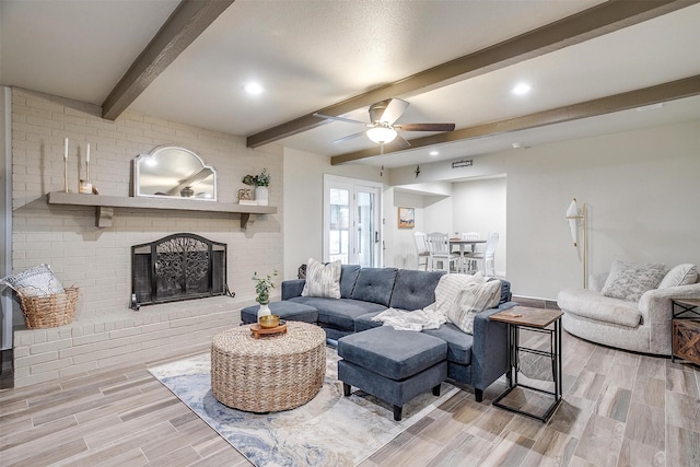 living room featuring beam ceiling, a brick fireplace, and ceiling fan