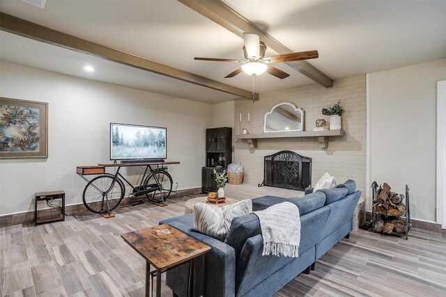 living room with beam ceiling, ceiling fan, light hardwood / wood-style floors, and a brick fireplace