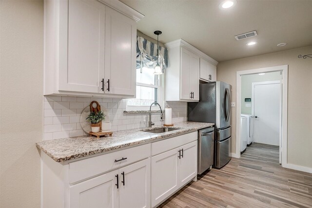 kitchen featuring washing machine and clothes dryer, white cabinetry, sink, and appliances with stainless steel finishes