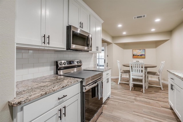 kitchen featuring backsplash, white cabinets, light hardwood / wood-style flooring, appliances with stainless steel finishes, and light stone counters