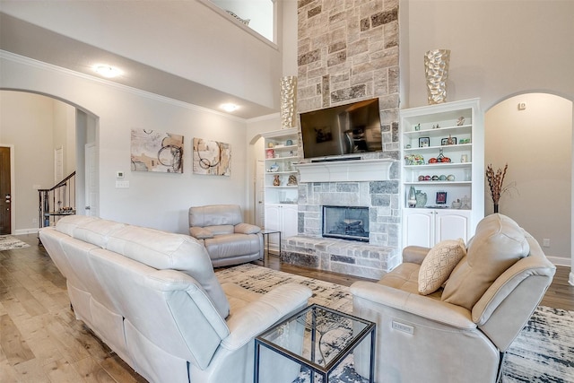 living room featuring a fireplace, ornamental molding, a high ceiling, and light wood-type flooring