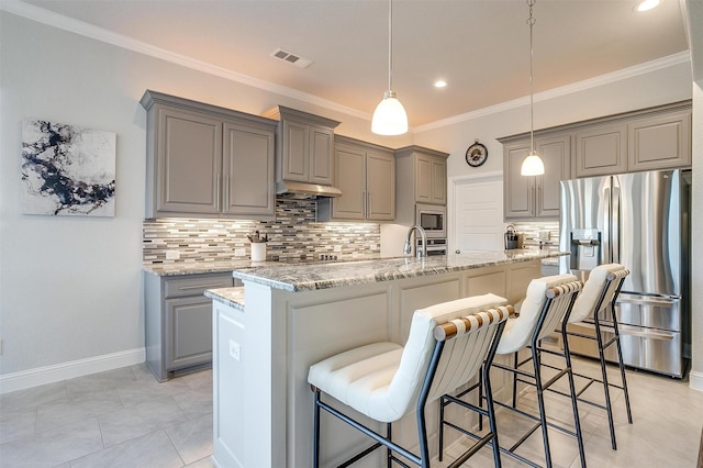 kitchen with light stone counters, a kitchen breakfast bar, an island with sink, pendant lighting, and stainless steel appliances