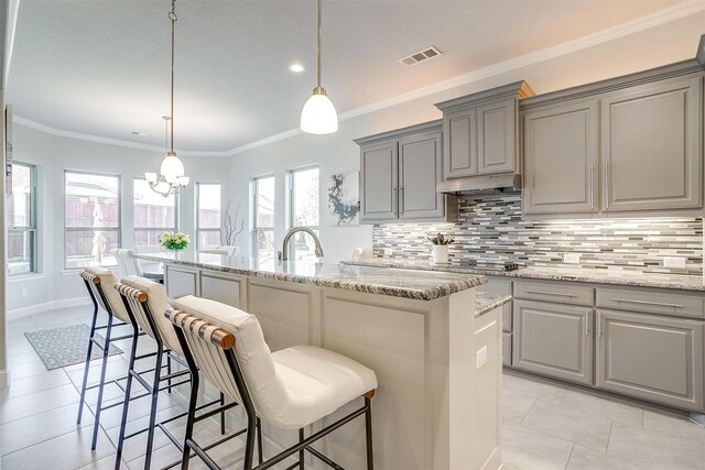 kitchen featuring tasteful backsplash, decorative light fixtures, light stone countertops, and a center island with sink