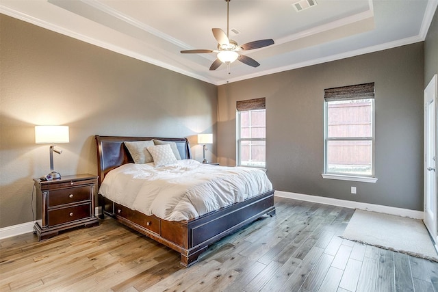 bedroom with crown molding, a tray ceiling, light hardwood / wood-style floors, and ceiling fan