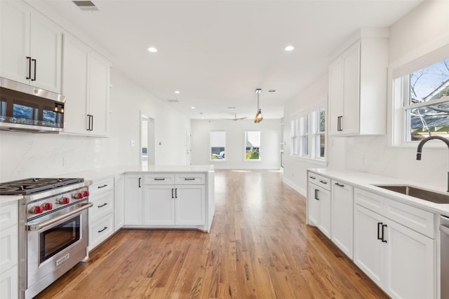 kitchen with kitchen peninsula, appliances with stainless steel finishes, white cabinetry, and sink