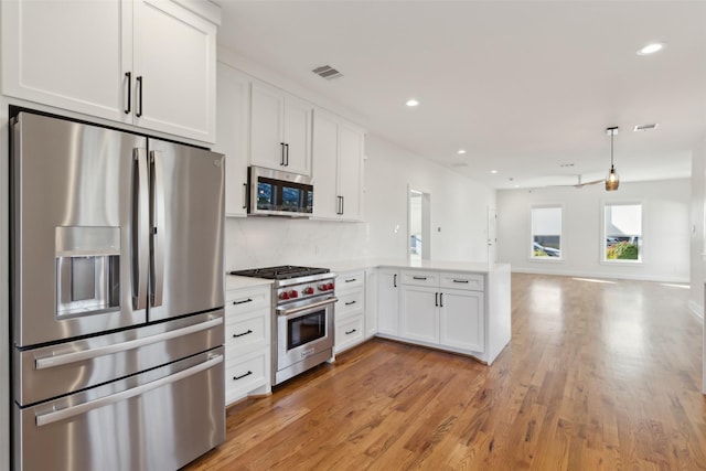 kitchen with white cabinets, decorative backsplash, light wood-type flooring, appliances with stainless steel finishes, and kitchen peninsula