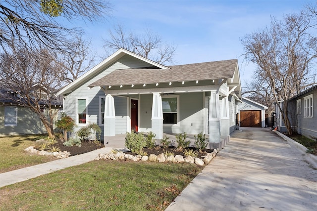 bungalow-style house featuring a porch, a garage, a front lawn, and an outdoor structure