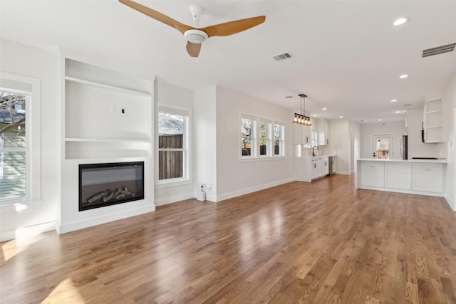 unfurnished living room featuring ceiling fan, hardwood / wood-style floors, and sink