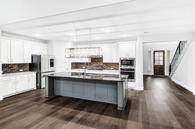 kitchen featuring an island with sink, pendant lighting, decorative backsplash, white cabinets, and appliances with stainless steel finishes