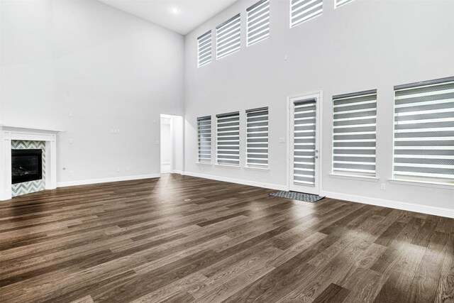 unfurnished living room featuring a high end fireplace, a towering ceiling, and dark hardwood / wood-style floors