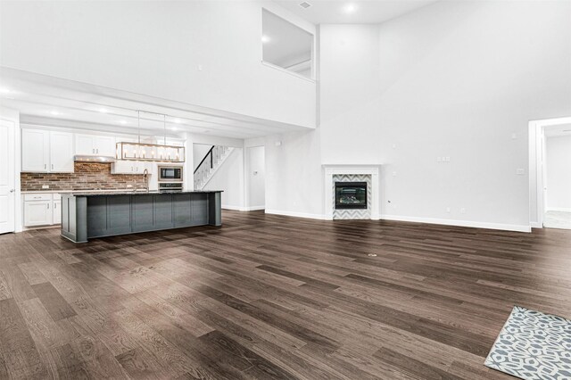 unfurnished living room with a fireplace, a towering ceiling, and dark hardwood / wood-style floors