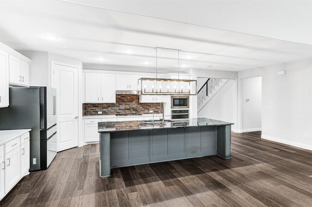 kitchen featuring stainless steel appliances, white cabinetry, an island with sink, and hanging light fixtures