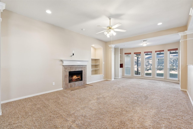 unfurnished living room with a tile fireplace, decorative columns, ceiling fan, light carpet, and built in shelves