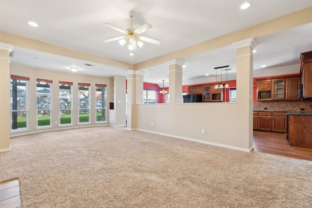 unfurnished living room featuring decorative columns, dark colored carpet, and ceiling fan