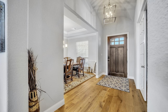 foyer entrance with crown molding, wood-type flooring, and an inviting chandelier