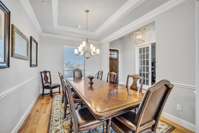 dining space featuring an inviting chandelier, light wood-type flooring, ornamental molding, and a tray ceiling