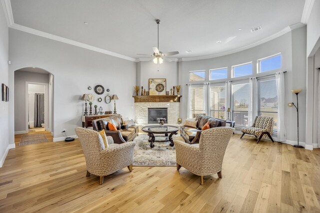 living room featuring ceiling fan, a towering ceiling, light hardwood / wood-style floors, a fireplace, and ornamental molding