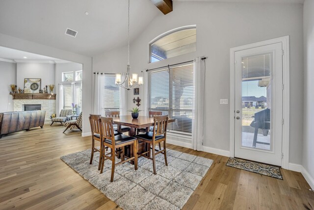 dining area featuring light wood-type flooring, lofted ceiling with beams, a stone fireplace, and a notable chandelier