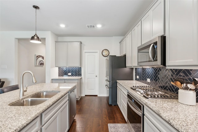 kitchen with backsplash, sink, appliances with stainless steel finishes, decorative light fixtures, and light stone counters