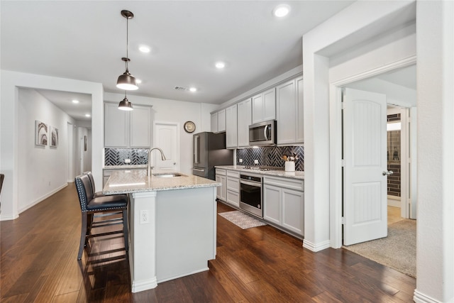 kitchen with decorative backsplash, appliances with stainless steel finishes, light stone counters, sink, and pendant lighting