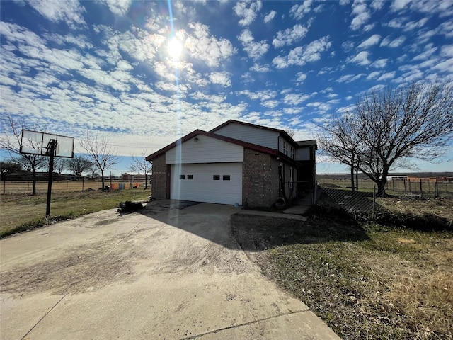 view of property exterior with a garage, driveway, brick siding, and fence