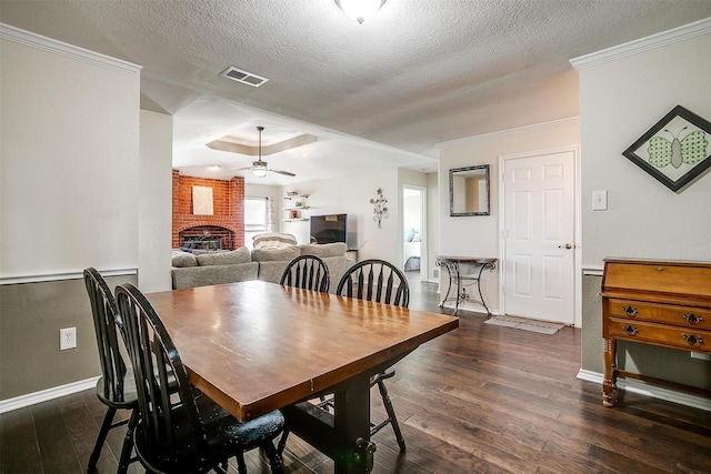 dining area featuring ceiling fan, dark hardwood / wood-style flooring, crown molding, and a brick fireplace