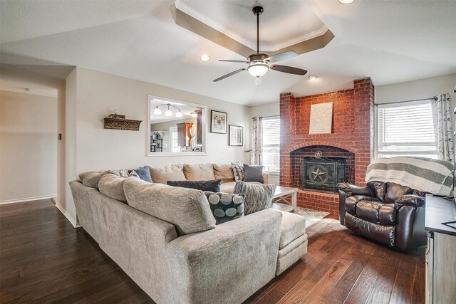 living room featuring ceiling fan, dark wood-type flooring, a raised ceiling, a fireplace, and ornamental molding