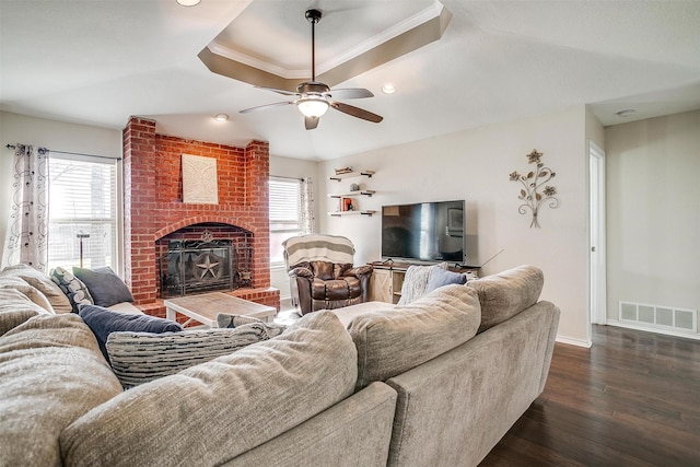 living room with a raised ceiling, a brick fireplace, ceiling fan, ornamental molding, and dark hardwood / wood-style flooring