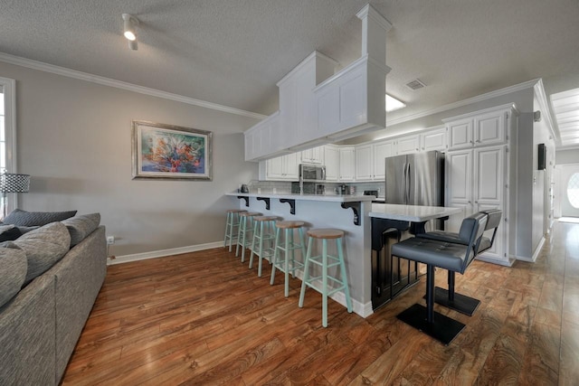 kitchen featuring kitchen peninsula, appliances with stainless steel finishes, a breakfast bar, dark wood-type flooring, and white cabinets