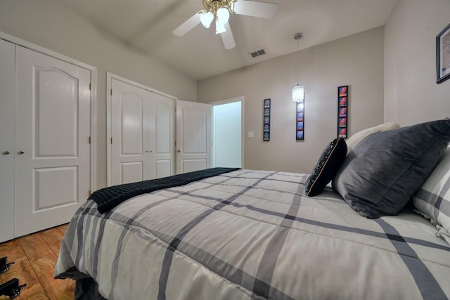 bedroom with a textured ceiling, light wood-type flooring, ceiling fan, and multiple closets