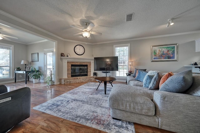 living room featuring ceiling fan, ornamental molding, a textured ceiling, and a brick fireplace