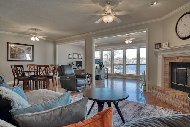 living room with ceiling fan, crown molding, a textured ceiling, and a brick fireplace