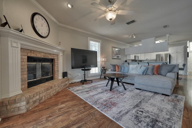 living room with ceiling fan, light hardwood / wood-style floors, a textured ceiling, a fireplace, and ornamental molding