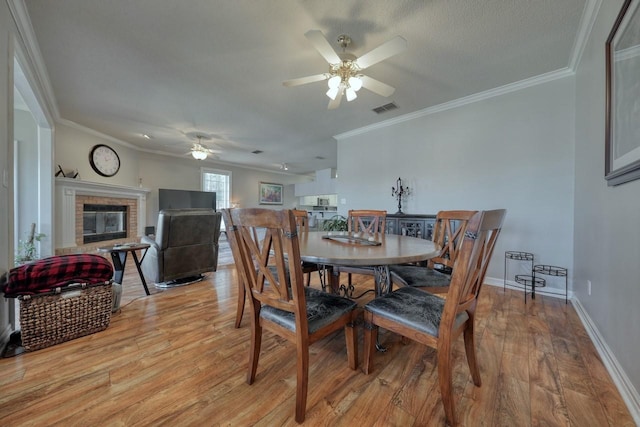 dining space featuring light hardwood / wood-style floors, a brick fireplace, ceiling fan, and ornamental molding