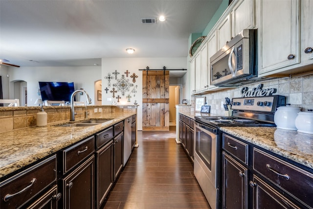 kitchen featuring appliances with stainless steel finishes, tasteful backsplash, sink, a barn door, and white cabinetry