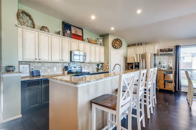 kitchen featuring a center island with sink, white cabinets, vaulted ceiling, and appliances with stainless steel finishes