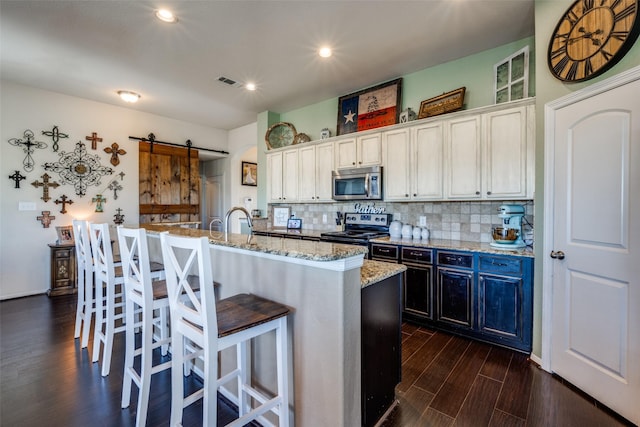 kitchen with white cabinets, a barn door, stainless steel appliances, and a center island with sink