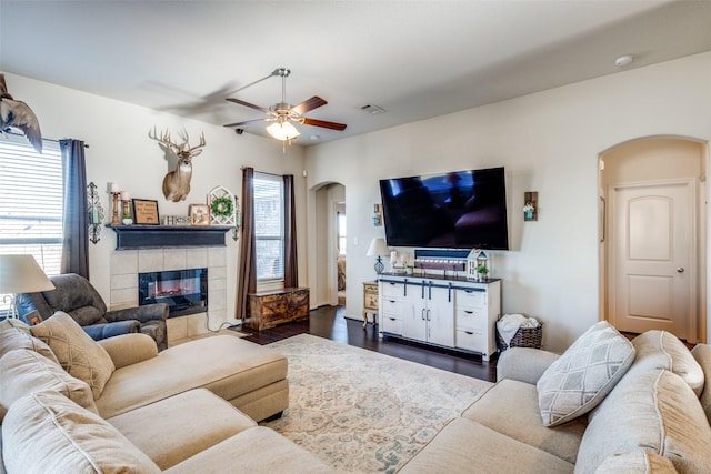 living room featuring dark hardwood / wood-style flooring, ceiling fan, and a tiled fireplace