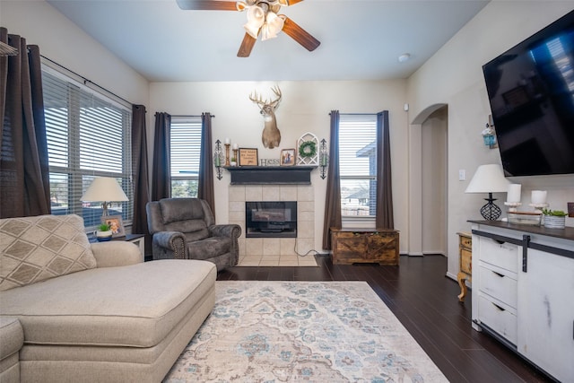 living room featuring plenty of natural light, ceiling fan, dark hardwood / wood-style flooring, and a tiled fireplace