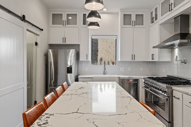 kitchen with exhaust hood, white cabinets, sink, a barn door, and appliances with stainless steel finishes