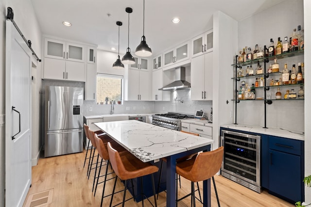 kitchen featuring a center island, beverage cooler, stainless steel appliances, wall chimney range hood, and a barn door