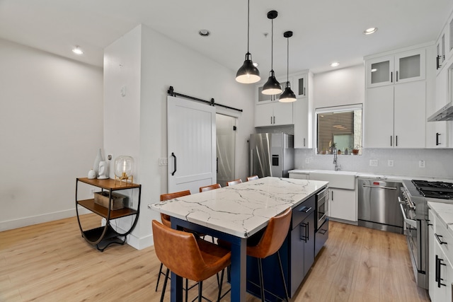 kitchen with stainless steel appliances, a barn door, a center island, white cabinetry, and hanging light fixtures