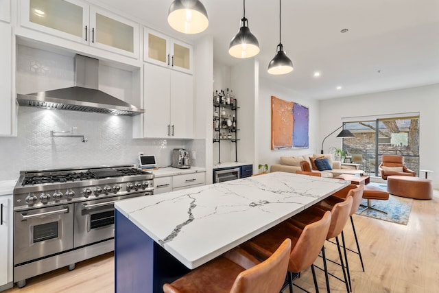 kitchen with light stone counters, a kitchen island, wall chimney range hood, double oven range, and white cabinetry