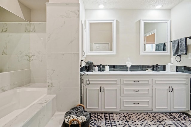 bathroom with a textured ceiling, vanity, and tiled tub