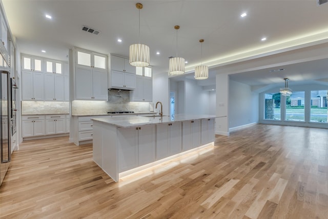 kitchen with light stone countertops, hanging light fixtures, light hardwood / wood-style flooring, a center island with sink, and white cabinets