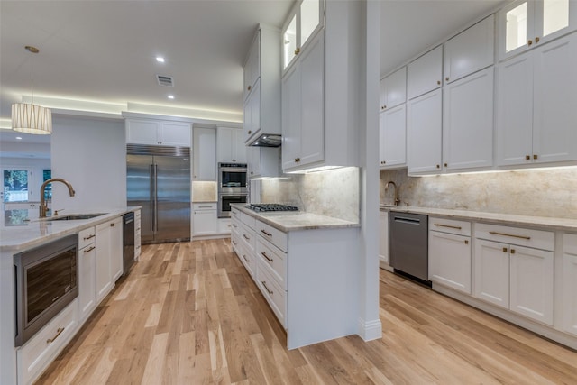 kitchen featuring sink, built in appliances, decorative backsplash, decorative light fixtures, and white cabinetry