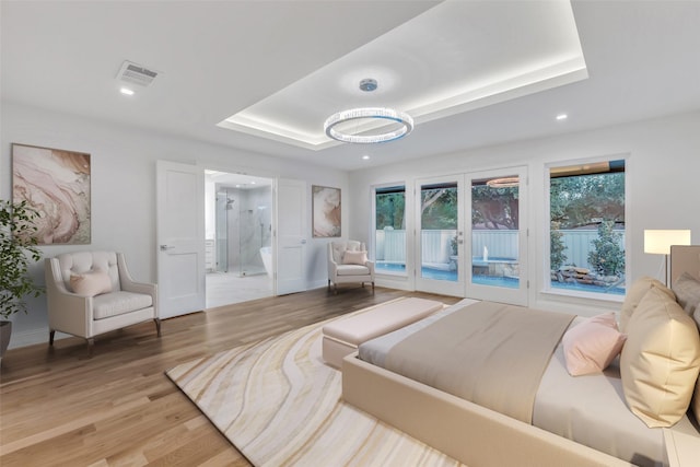 bedroom with wood-type flooring, french doors, connected bathroom, and a tray ceiling